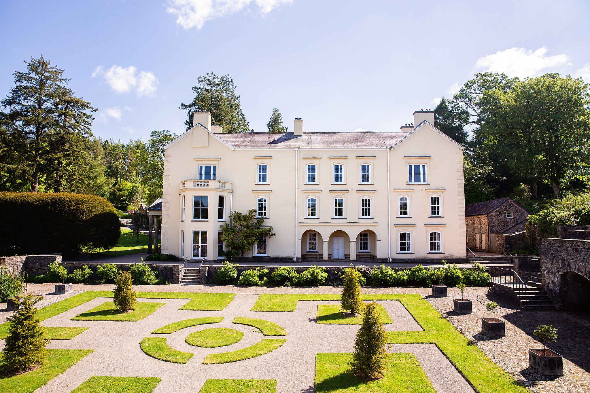 Manicured lawns and shrubbery outside of a white manor house.
