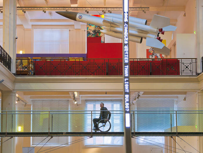 رجل على كرسي متحرك على ممر مرتفع في متحف ينظر إلى المعروضات