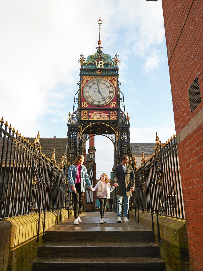 A family of three look out over a town from a clocktower bridge.