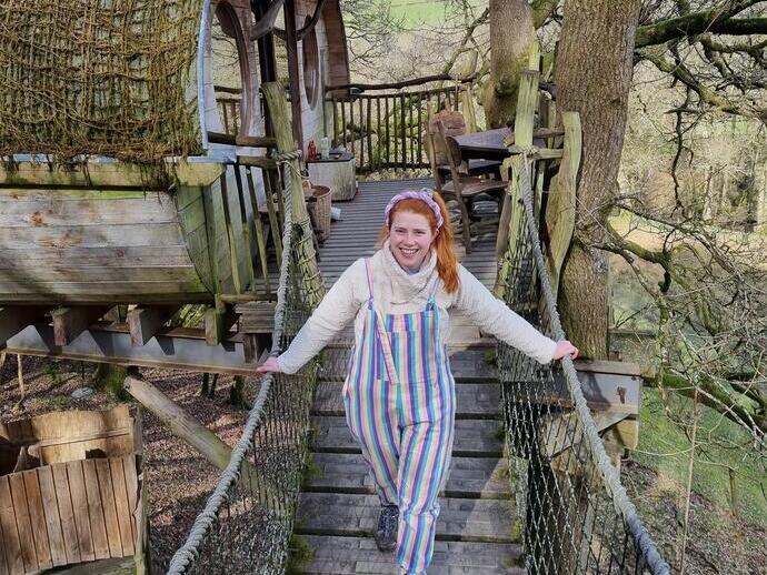 Junge Frau, die von einem Baumhaus aus über eine Seilbrücke geht