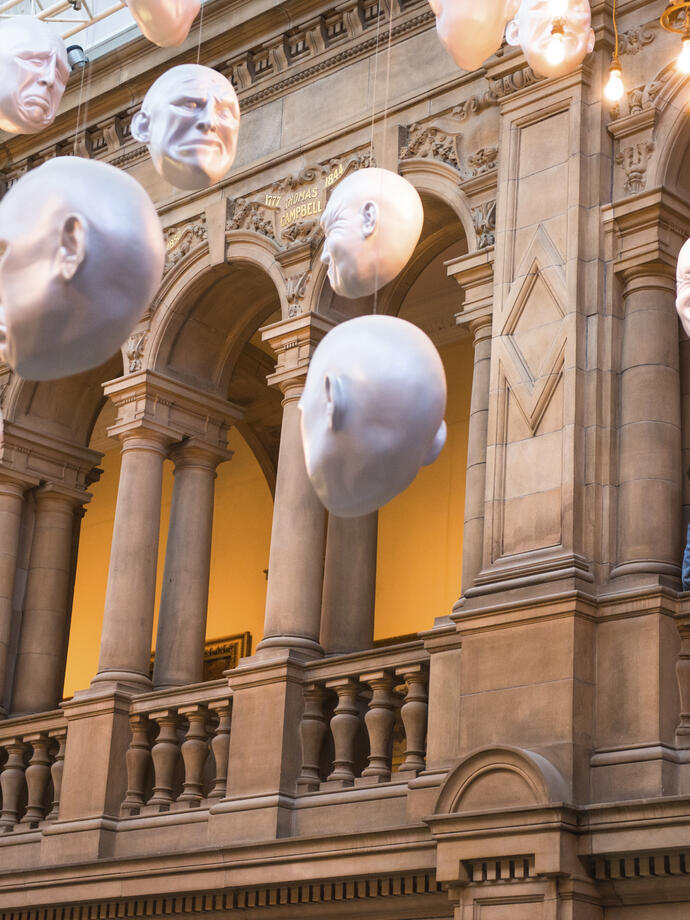 Two men looking at installation of suspended head sculptures inside a museum.