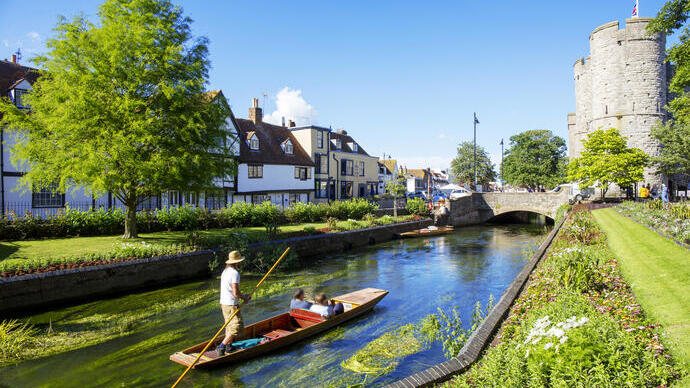 Un hombre y una pareja en una barca en un pequeño río rodeado de jardines y casas