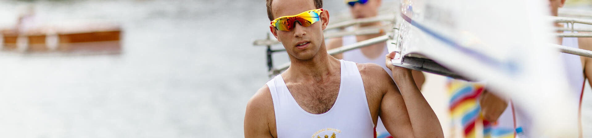 Rowers carrying a racing scull by the side of a river