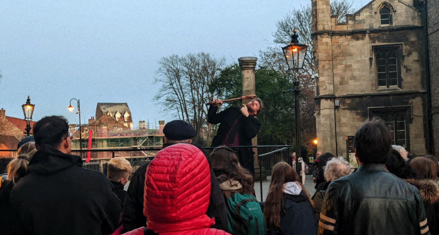 A costumed tour guide on a raised platform in front of an audience next to a historic building.