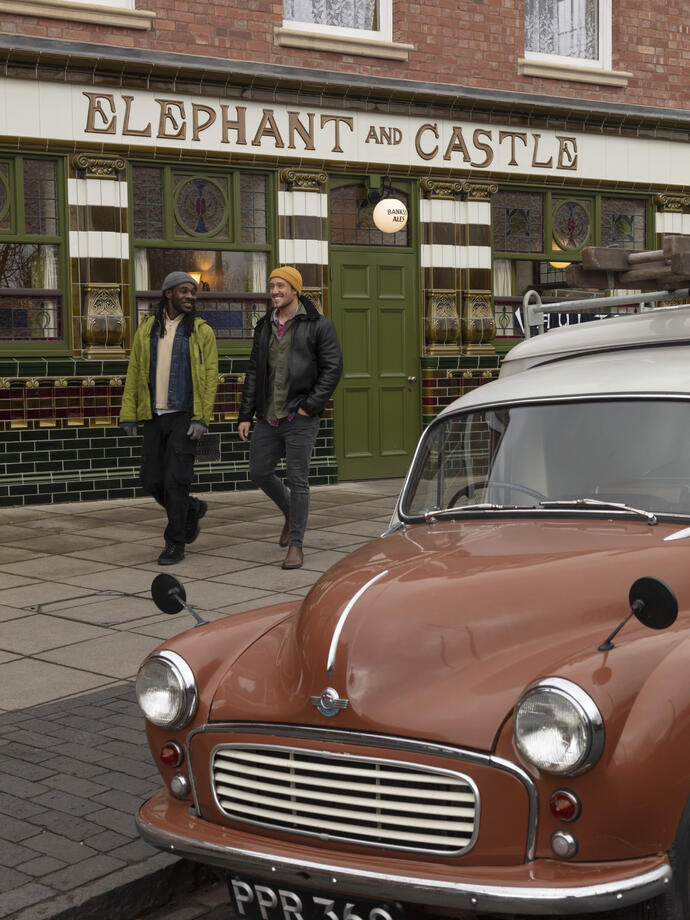 Three men walking past an old English pub with a vintage car out the front.