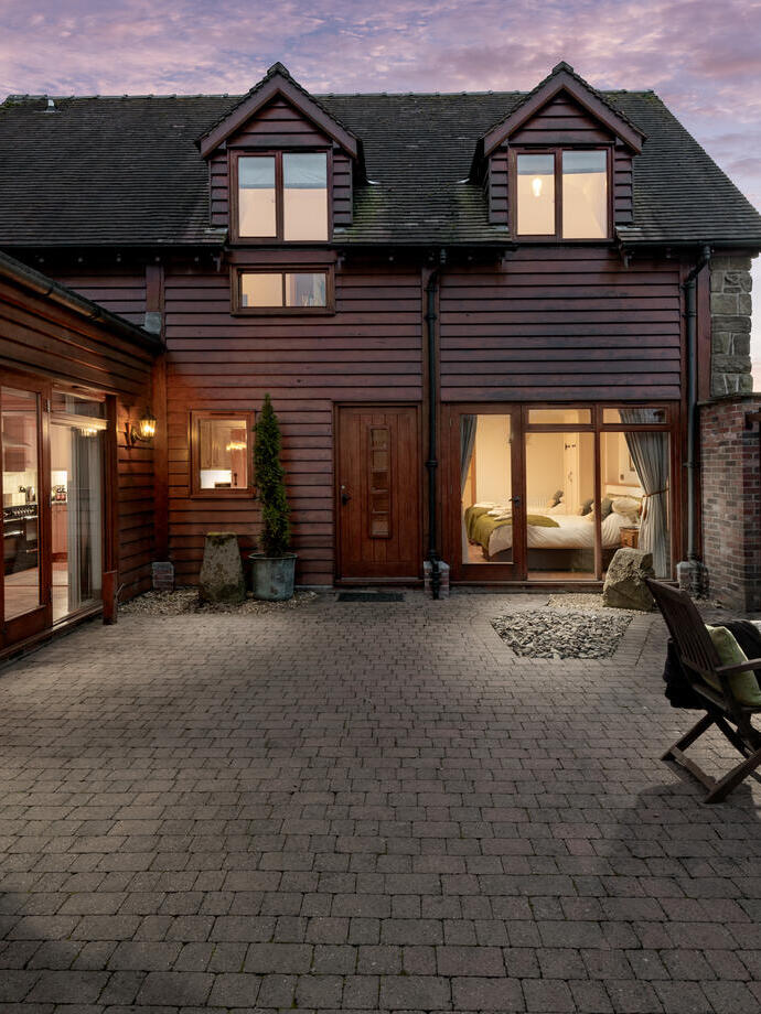 A wood clad building with two sets of French doors and a brick covered patio area in front with a table and chairs. Eaton Manor Country Estate - Bronze award winner for Self Catering Accommodation of the Year at the VisitEngland Awards for Excellence 2023.