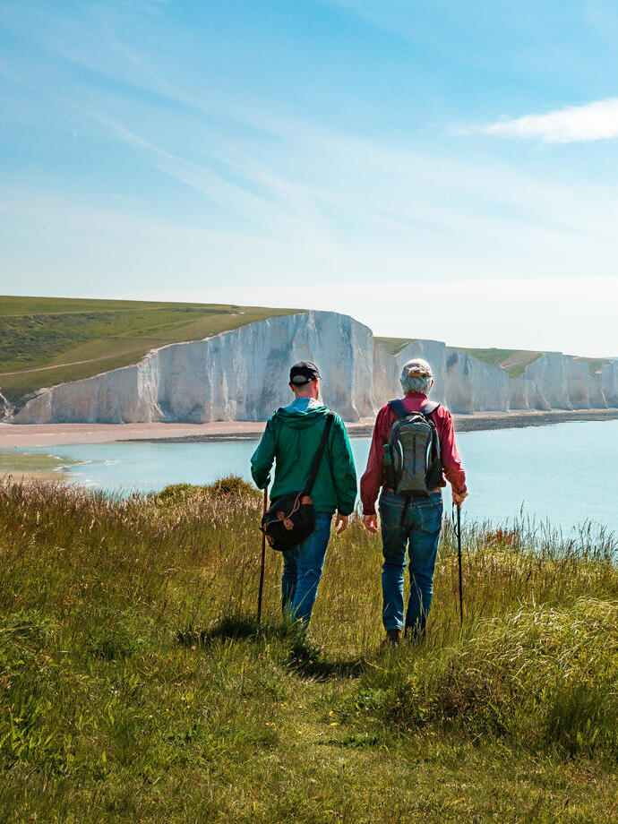 Two men hiking together with the stunning backdrop of white cliffs overlooking the ocean.
