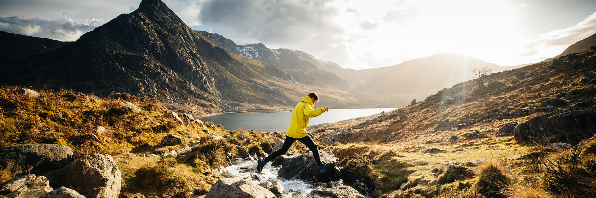 رجل يقفز من صخرة إلى أخرى عبر جدول مائي يتدفق إلى بحيرة