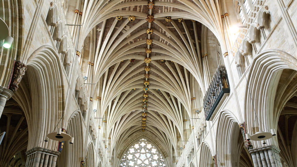 Das Gewölbe einer gotischen Kathedrale mit kunstvollen Steinmetzarbeiten und dekorativen Schlusssteinen, vom Kirchenschiff aus gesehen.