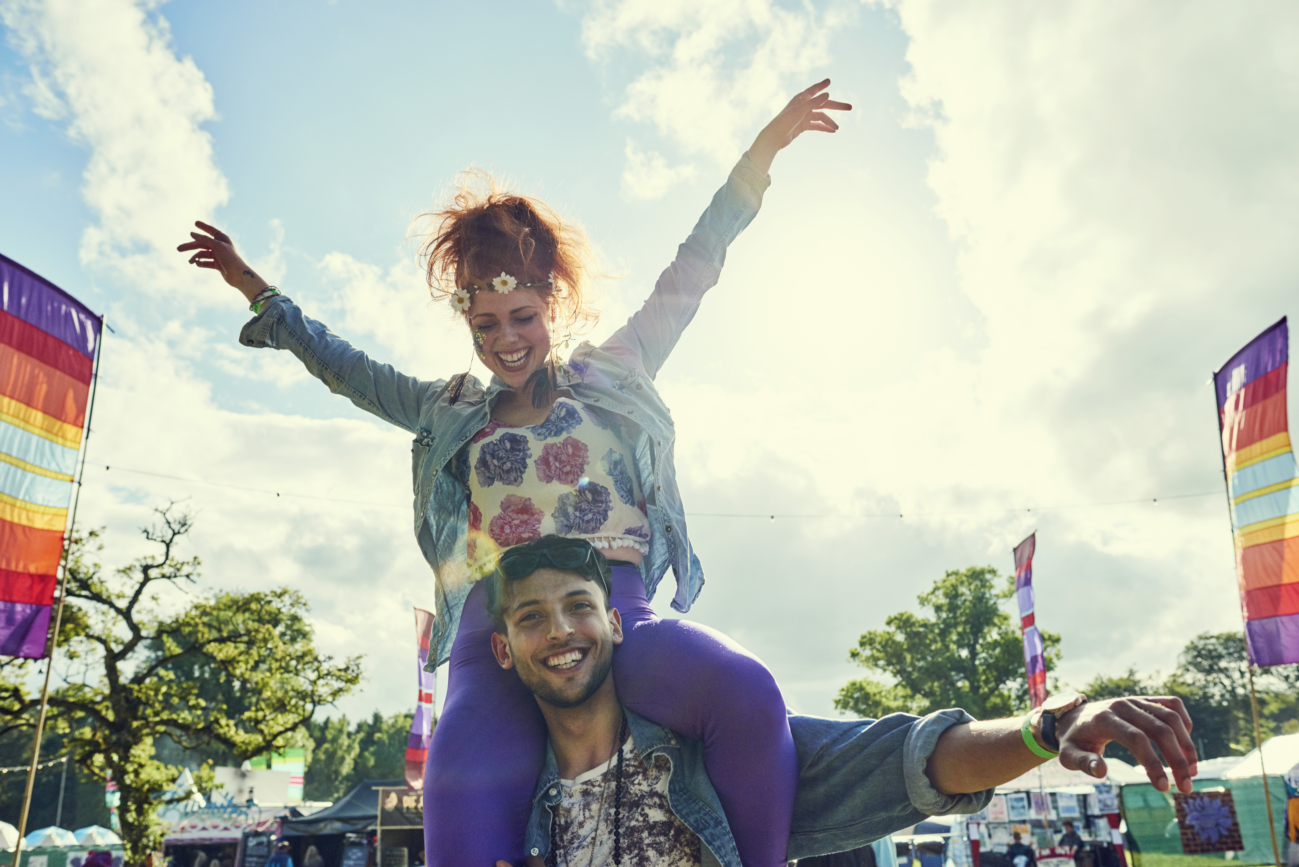 A woman sits on a man's shoulders at a festival in the summertime