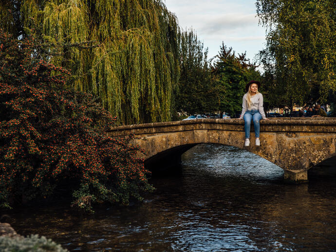 Woman sitting on low bridge over a river in a village