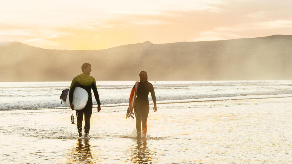 Man and woman, carrying surfboards and walking out of the sea