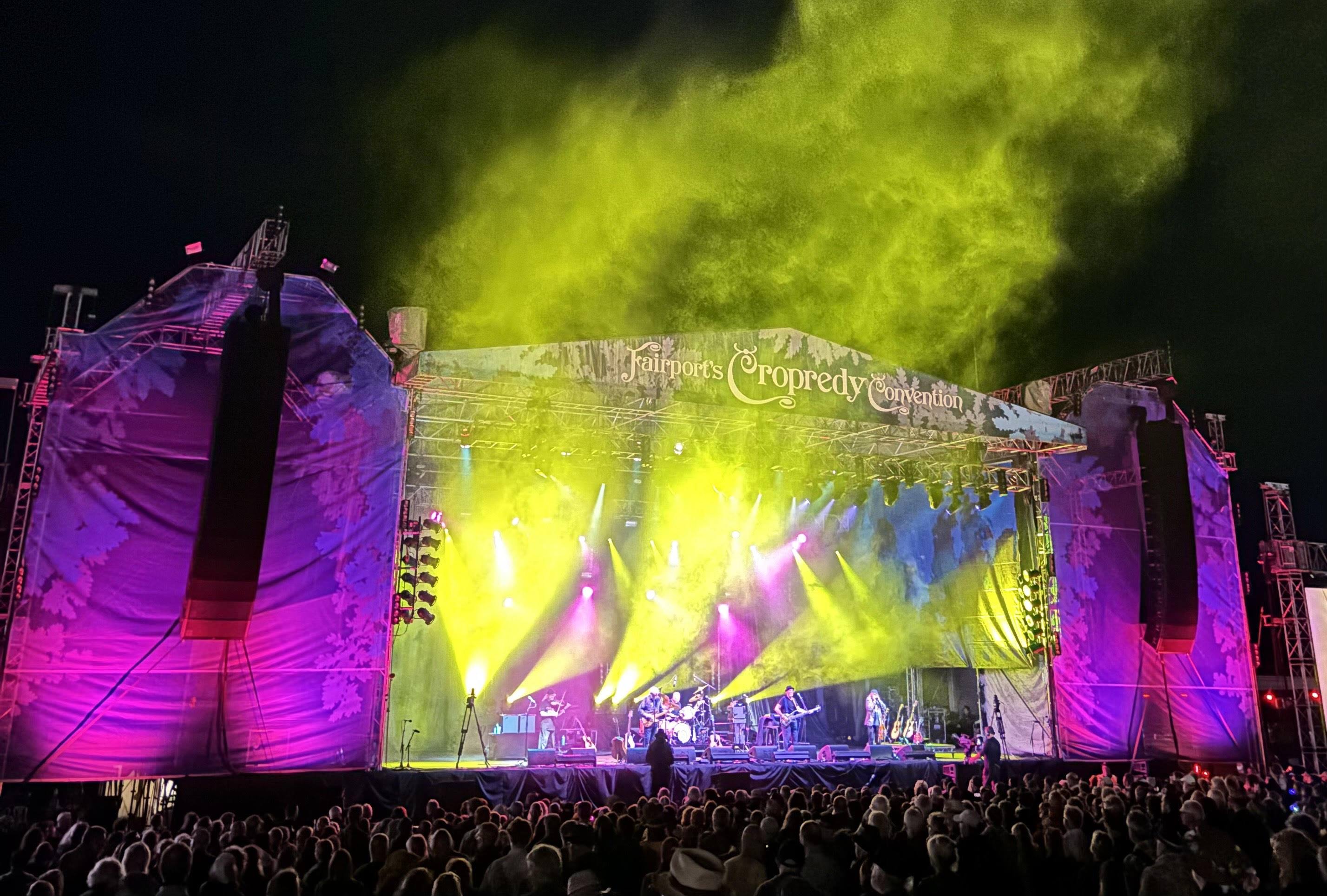 A crowd of people in front of the stage of a musical festival at night. 