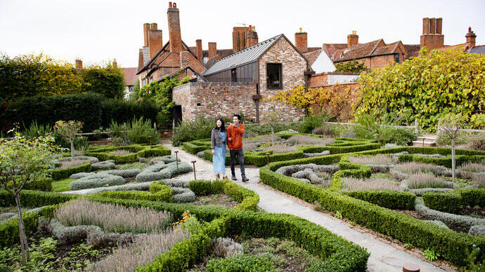 Couple walking through the knot garden of a large house