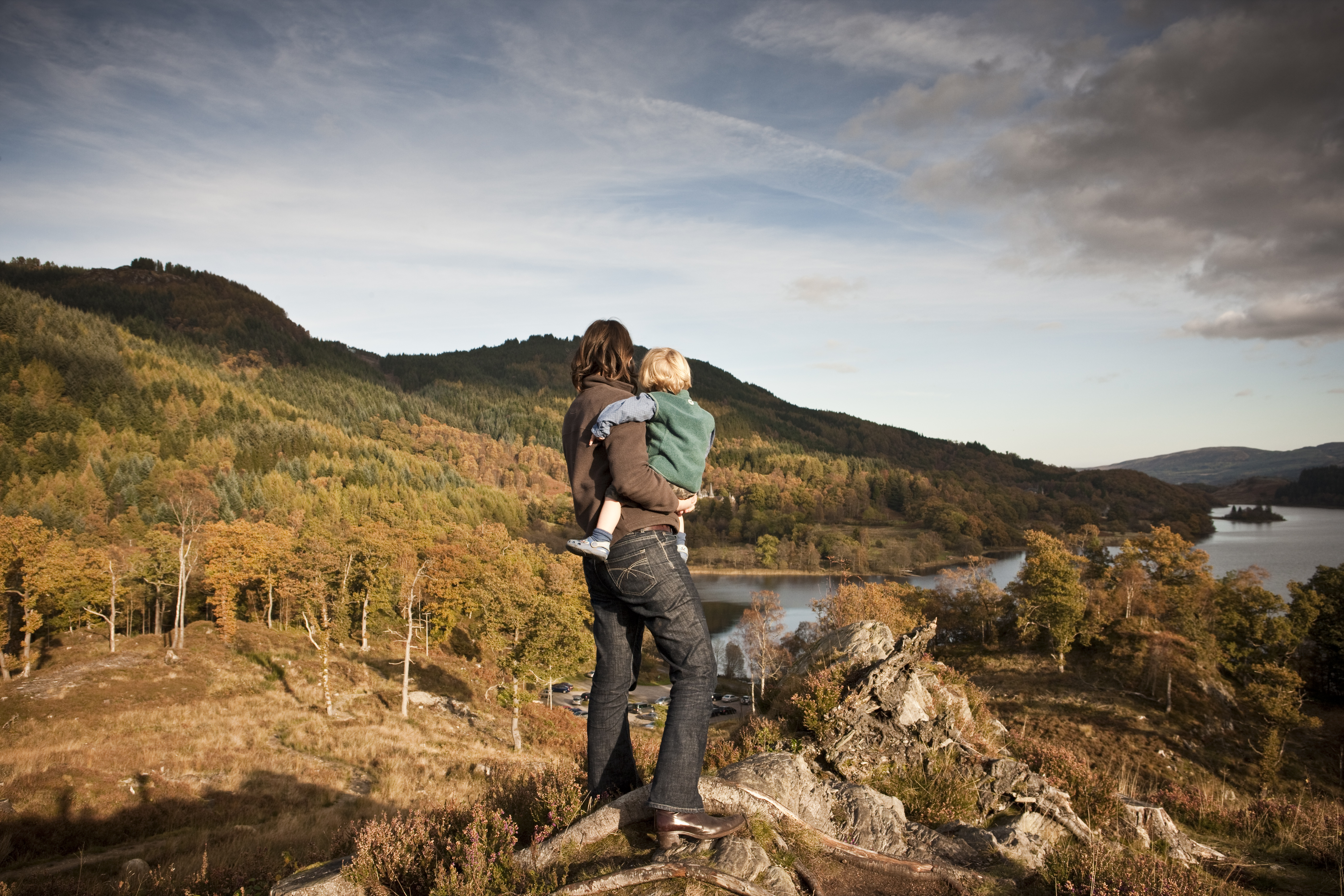Woman and child standing on a hilltop overlooking a lake.