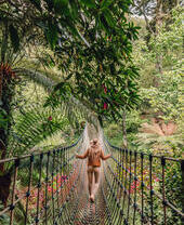 Une femme traversant un pont suspendu entouré d'arbres