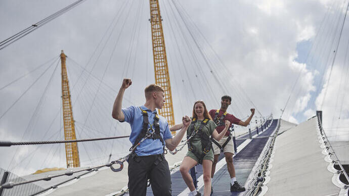 Two men and a woman walking down the side of a stadium roof wearing safety harnesses