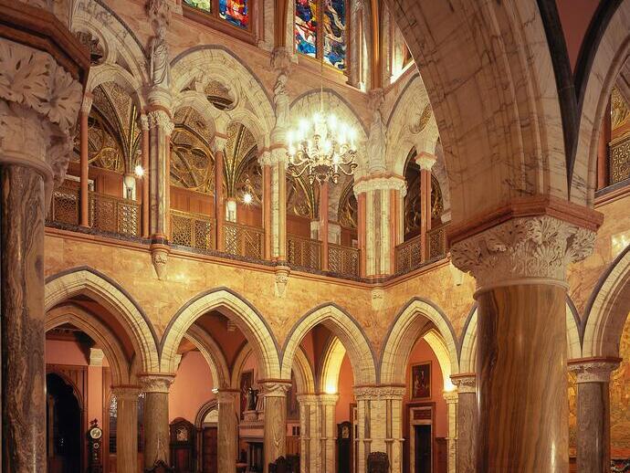 Inside a large marble hall and stained glass windows of a stately mansion.