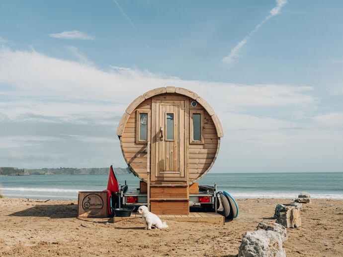 A purpose built beach sauna parked on the sand by the ocean's edge.