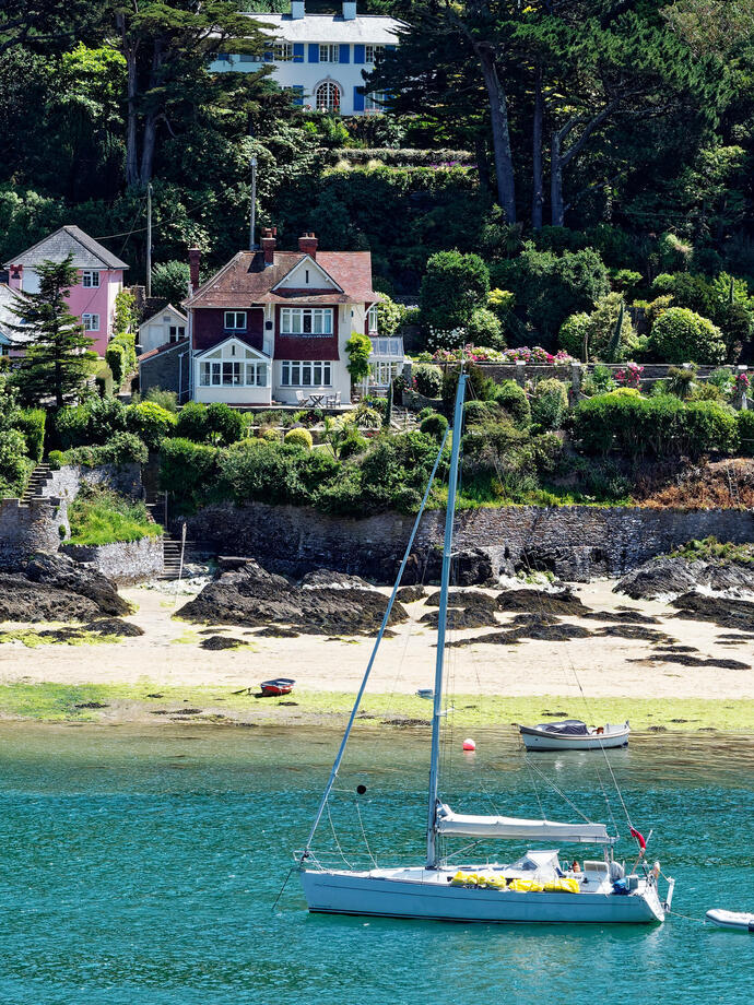 A sailing yacht in a quiet harbour with houses in the background