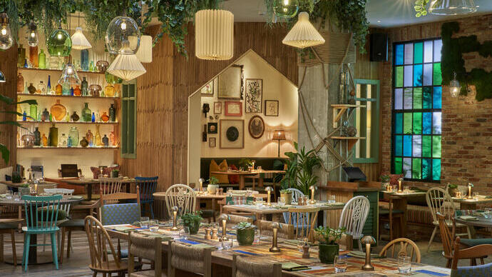 Tables set inside a restaurant with hanging lamps and green foliage.