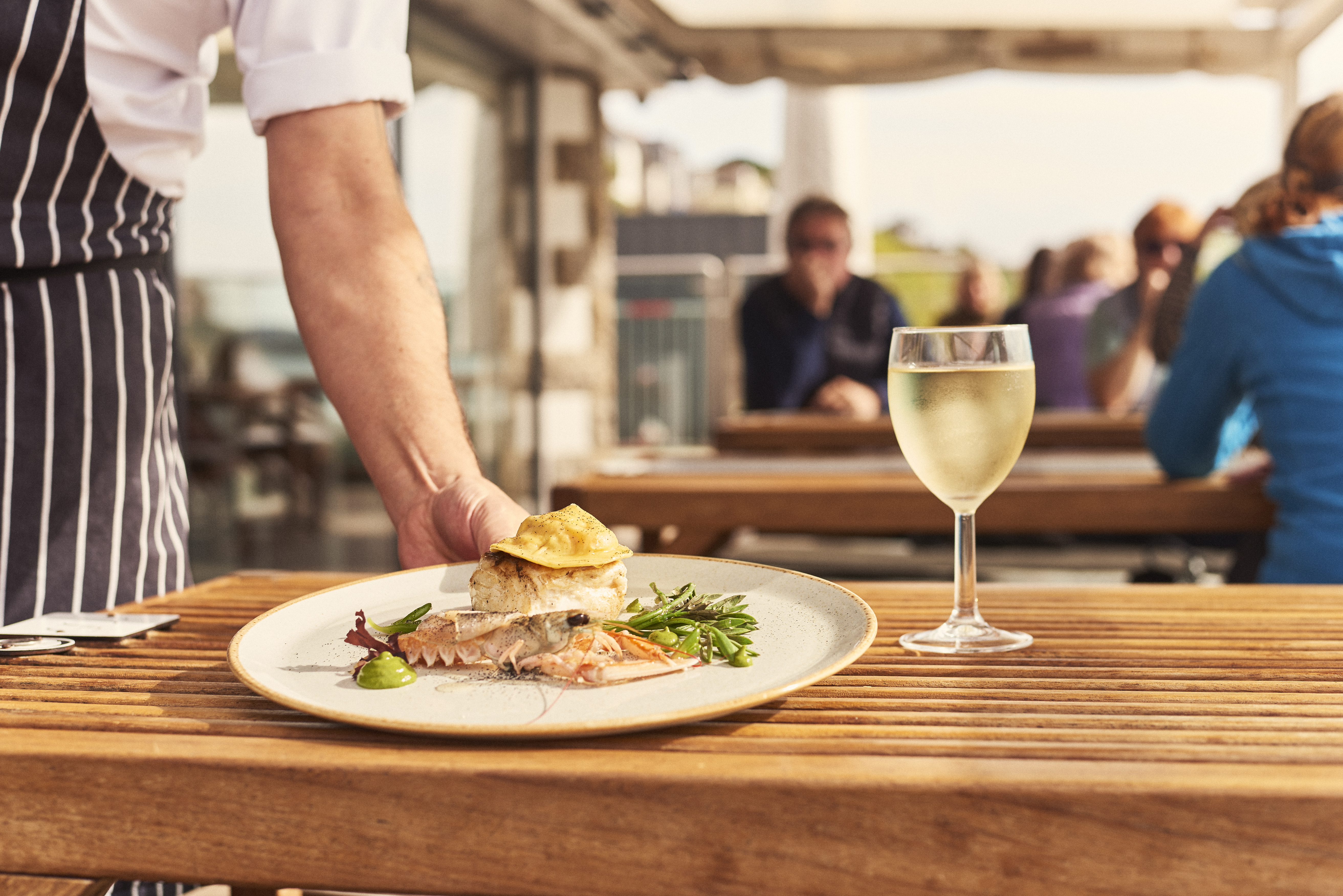 Waiter placing plate of food on table beside glass of wine