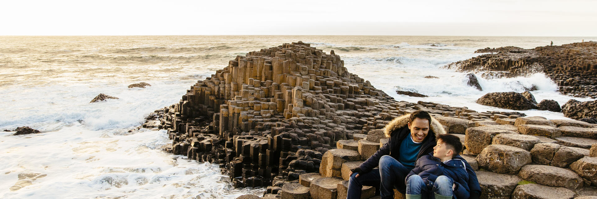 Man and child sitting on rock formations by the sea