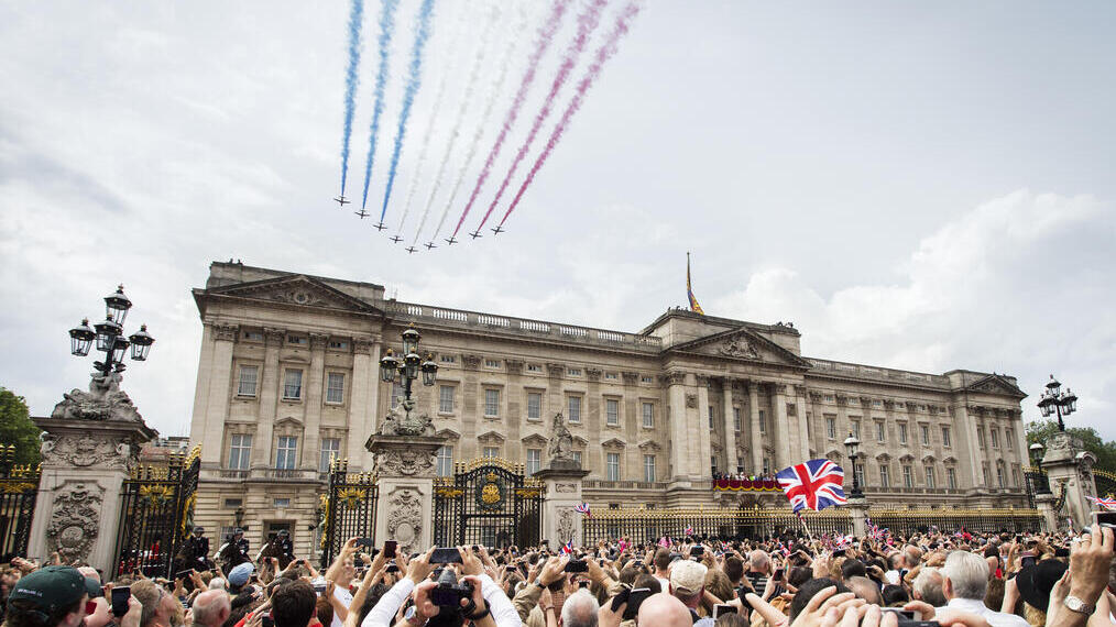 Jets with coloured smoke trailing behind fly in formation over crowds and a palace
