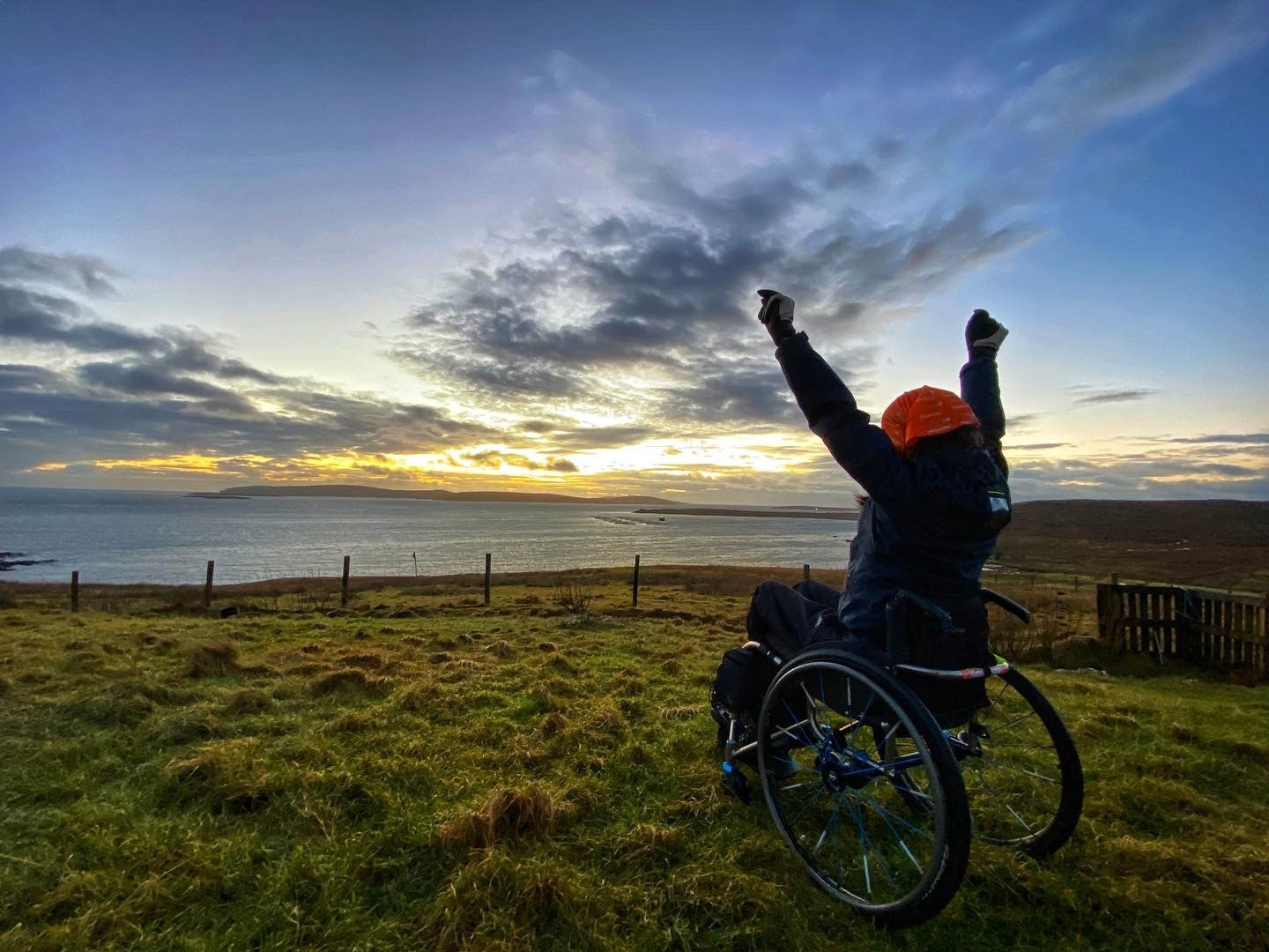 Wheelchair user, arms outstretched looking over the sea, watching the sunrise