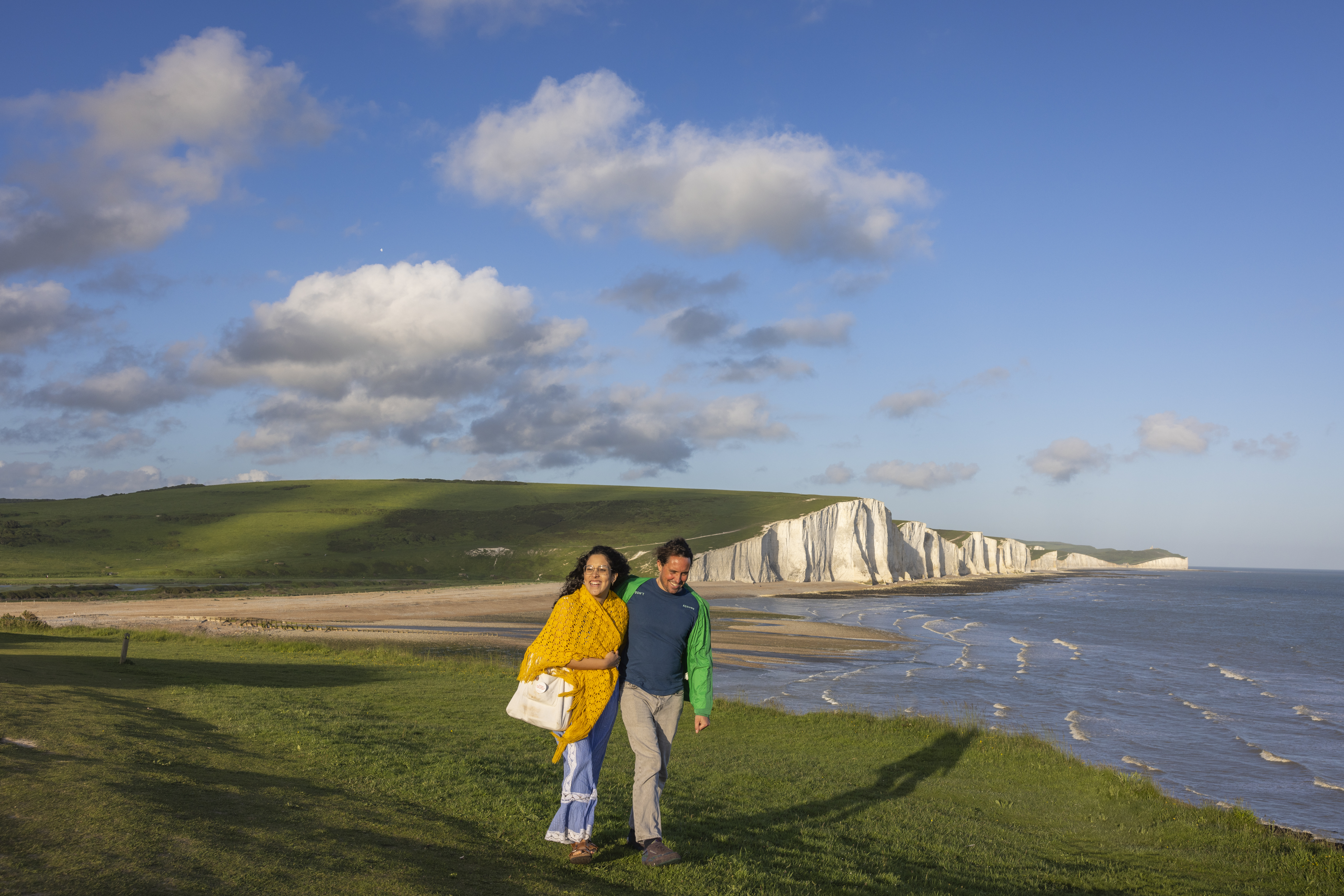 A woman and a man walk together on a headland with chalk cliffs beyond