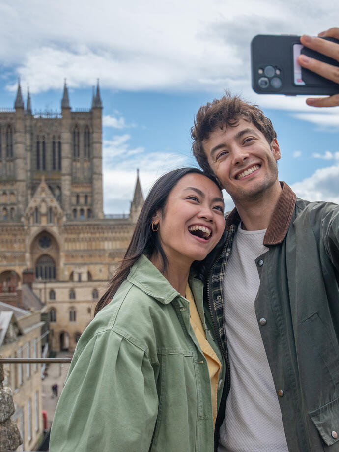 A man and woman smiling and taking a selfie in front of a Cathedral