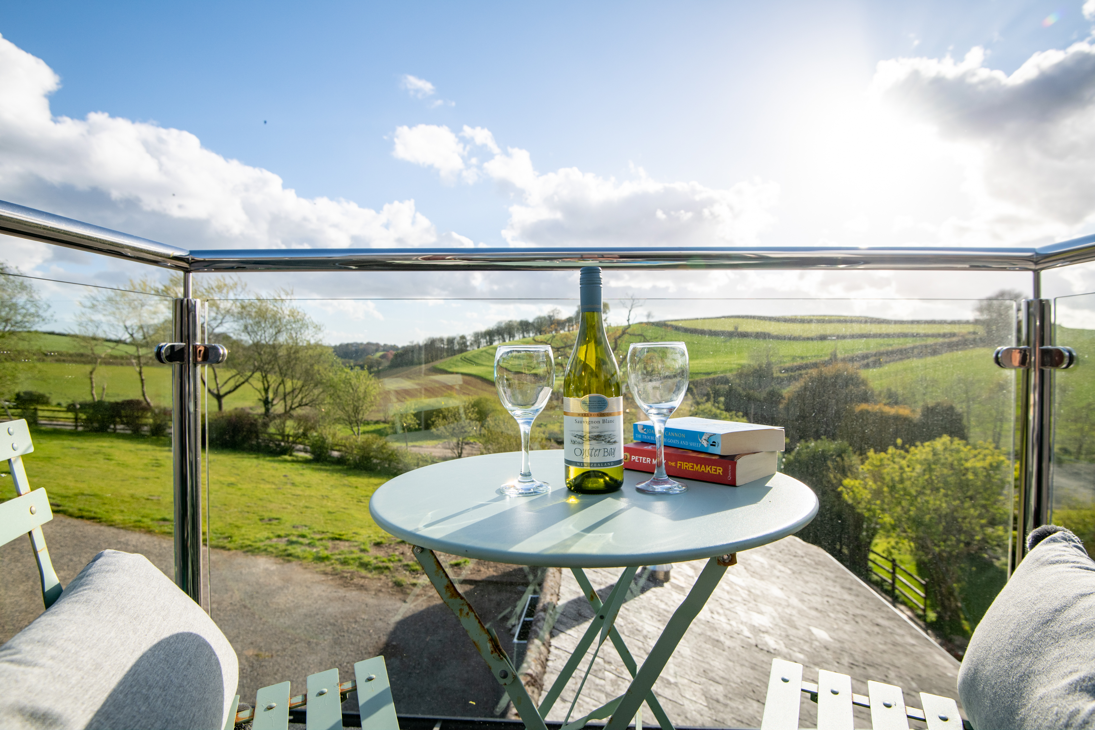 View from the balcony with a bistro table and chairs set with two novels, two wine glasses and a bottle of wine with a rural landscape in the background.