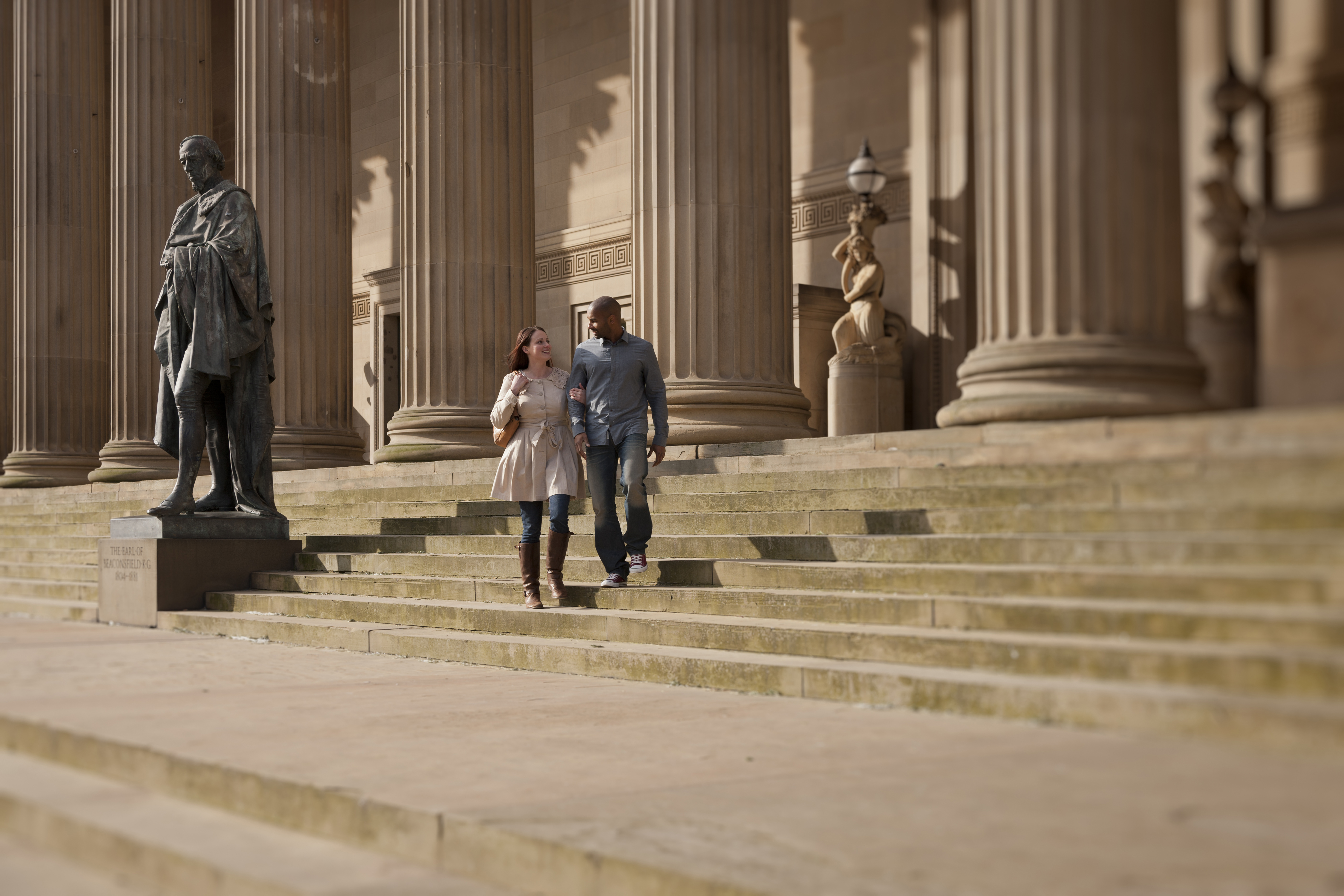 Couple walking past stone steps, columns and sculptures in a city square