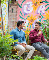 Due uomini seduti su una panchina in un giardino con un drink