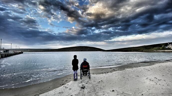 Wheelchair user and child on a beach looking out to sea