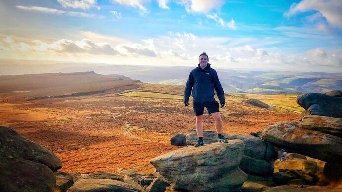 Ein Mann posiert auf dem Gipfel des Higger Tor mit weitem Blick auf den Peak District im Hintergrund