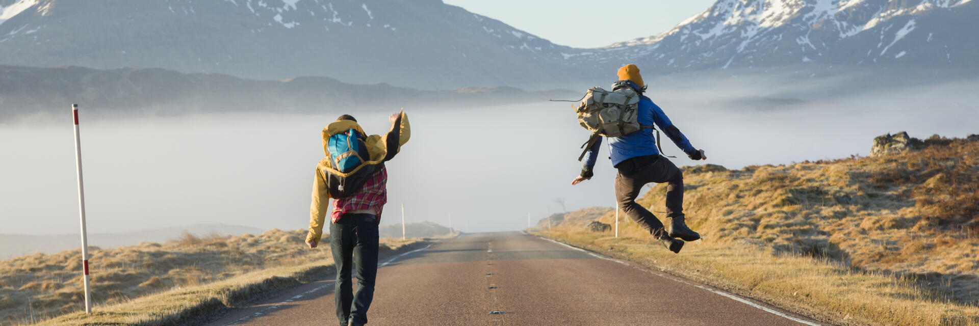 Two men walking and jumping on a road surrounded by mountains