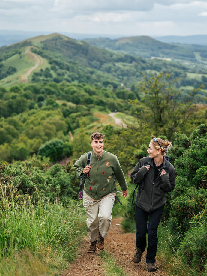 Two women walk up a pathway on a hill while carrying rucksacks