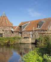 Un mulino ad acqua in pietra con un insolito tetto conico accanto a uno stagno.