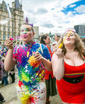 Dos personas celebrando el Orgullo de Liverpool soplando pompas de jabón hacia la cámara