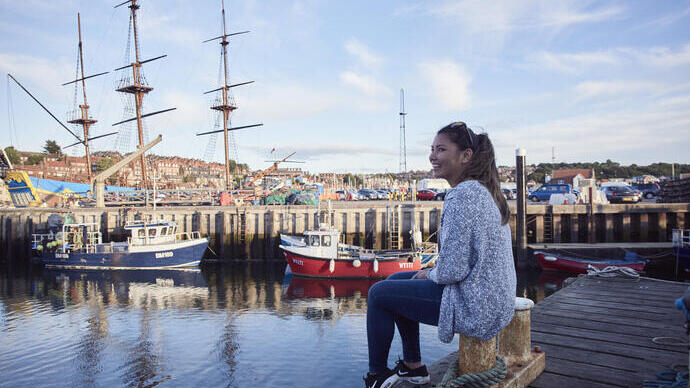 Femme souriante assise sur une jetée dans un port