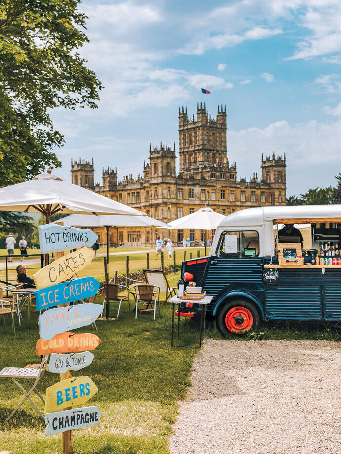 Food truck and direction signs at a festival at Highclere Castle with house behind