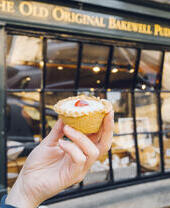 Hand holding Bakewell tart in front of bakery