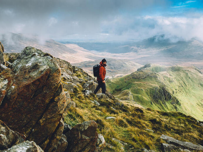 Ein robust gekleideter Mann, der den Gipfel einer großen Bergkette mit Panoramablick erklimmt.