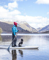 Woman and a dog on a paddleboard on a lake with mountains in the background