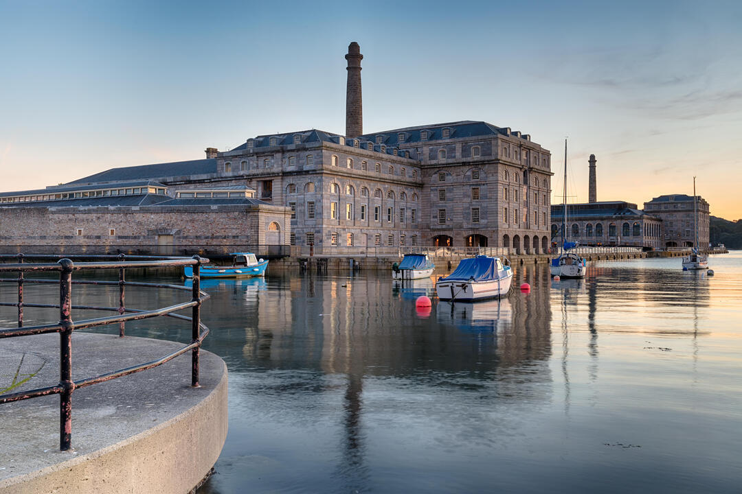 Dusk at a dock yard with small boats in foreground in the sea in front of a large industrial building