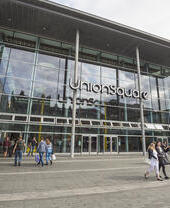 People carrying bags of shopping walking around outside of a modern shopping centre.