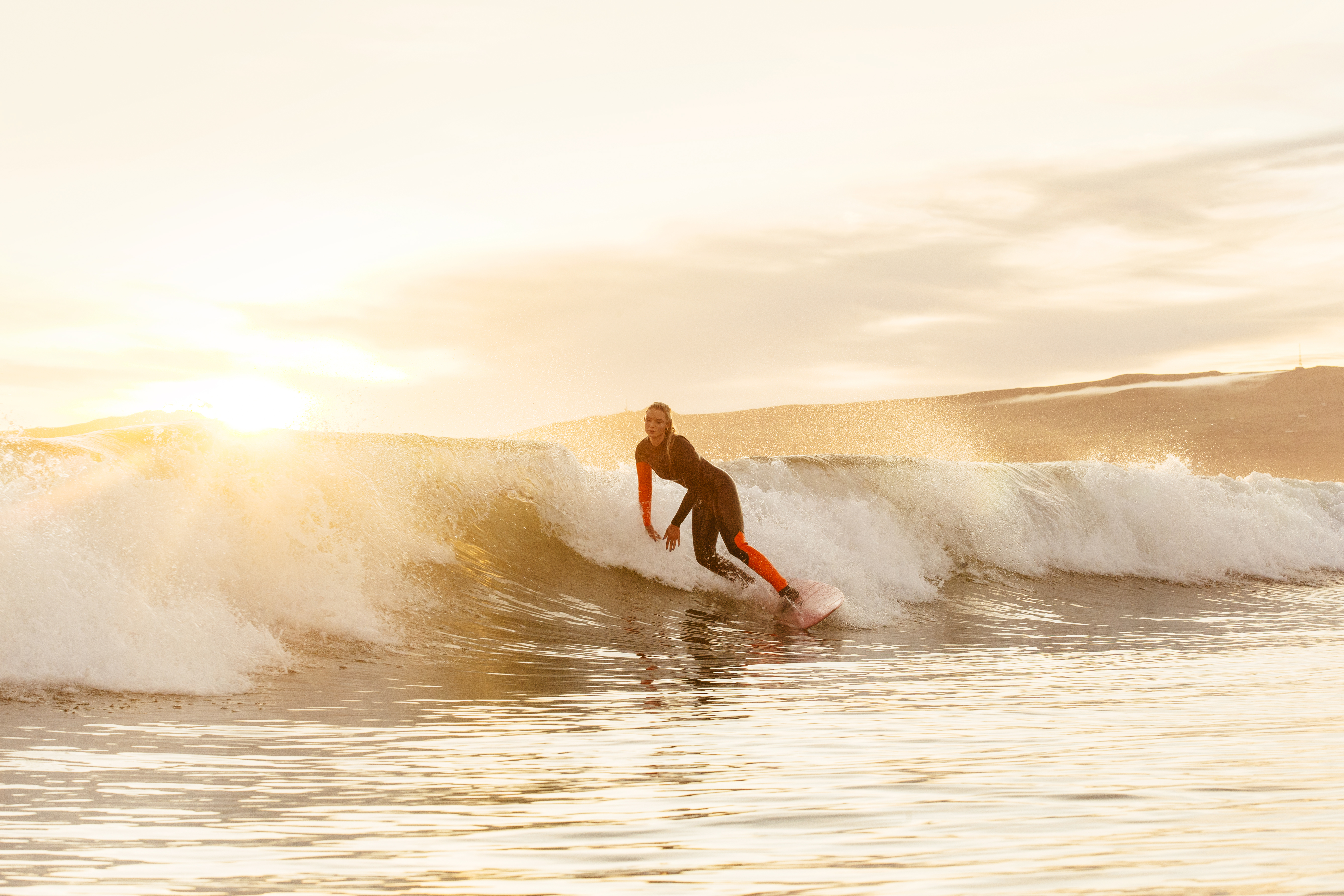 Woman, in black and red wetsuit, surfing a small wave in the sea
