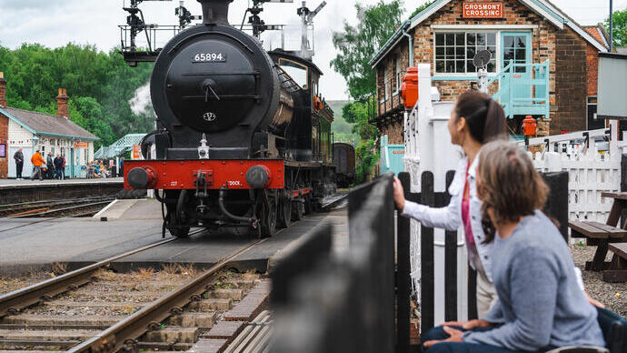Mann und Frau an einem Bahnhof, die einen historischen Zug vorbeifahren sehen, Mann im Rollstuhl