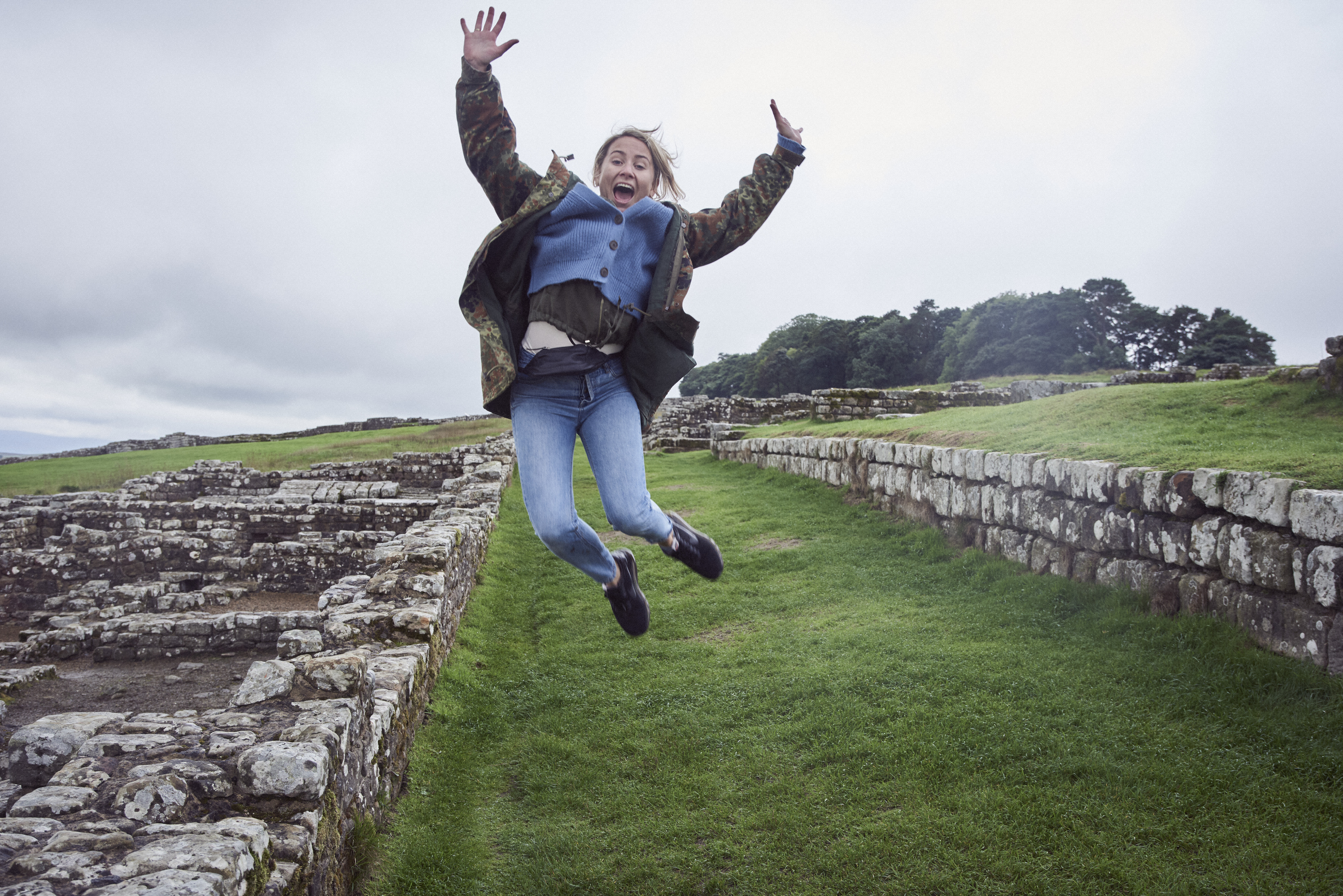 Niña saltando en el aire con los brazos levantados cerca de un muro de piedra